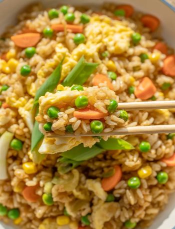 Colorful homemade fried rice with peas, carrots, corn, and scrambled eggs in white bowl with chopsticks