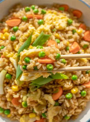Colorful homemade fried rice with peas, carrots, corn, and scrambled eggs in white bowl with chopsticks