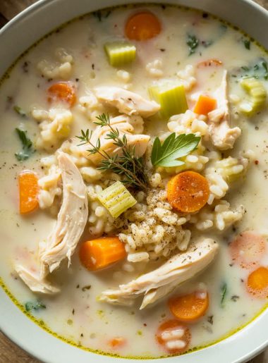 Close-up of creamy chicken and rice soup in a white bowl with visible carrots, celery, tender chicken pieces, and fresh herbs