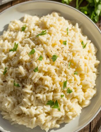 Close-up of creamy garlic parmesan rice in a white ceramic bowl, garnished with fresh chopped parsley and black pepper, with a silver fork on the side