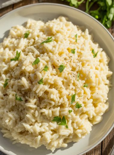 Close-up of creamy garlic parmesan rice in a white ceramic bowl, garnished with fresh chopped parsley and black pepper, with a silver fork on the side