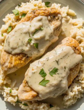 Creamy smothered chicken breasts covered in rich garlic cream sauce served over fluffy white rice, garnished with fresh parsley