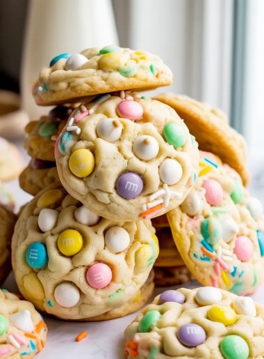 Soft chewy Easter cookies loaded with white chocolate chips pastel M&Ms and colorful Easter sprinkles piled together on a white marble surface