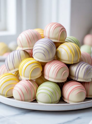 Easter egg shaped Oreo balls coated in white chocolate with colorful pastel pink purple yellow and green drizzles piled high on a white ceramic plate