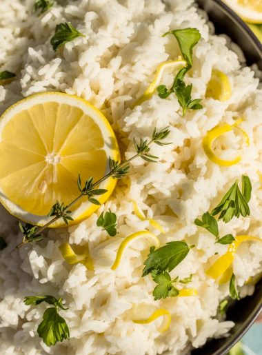 Fluffy Greek lemon rice with fresh herbs, lemon slices, and lemon zest in black serving bowl