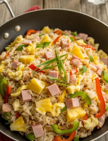 Colorful Hawaiian fried rice in a wok with chunks of pineapple, diced ham, bell peppers, and green onions garnish