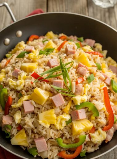 Colorful Hawaiian fried rice in a wok with chunks of pineapple, diced ham, bell peppers, and green onions garnish