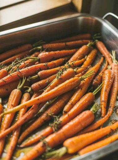Honey roasted carrots glazed and caramelized with golden edges in a stainless steel roasting pan garnished with fresh thyme