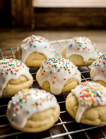 Soft glazed Italian Easter cookies topped with colorful nonpareil sprinkles cooling on a wire rack on a wooden surface