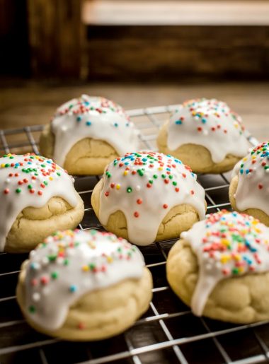 Soft glazed Italian Easter cookies topped with colorful nonpareil sprinkles cooling on a wire rack on a wooden surface
