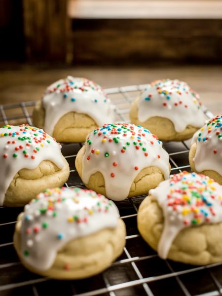 Soft glazed Italian Easter cookies topped with colorful nonpareil sprinkles cooling on a wire rack on a wooden surface