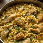 Golden seared chicken pieces and tender egg noodles in a rich creamy garlic butter sauce in a large skillet garnished with fresh parsley
