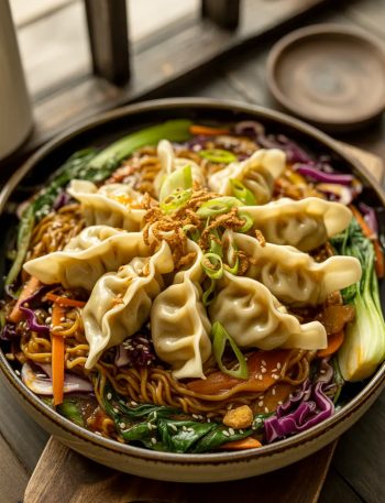 Potsticker noodle bowl loaded with crispy golden pan-fried potstickers over stir-fried noodles colorful vegetables and savory garlic ginger sauce garnished with green onions and sesame seeds