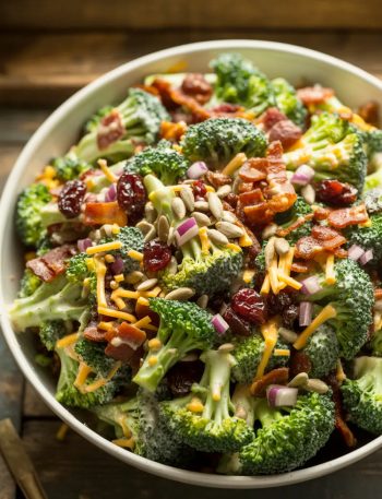 The best broccoli salad in a large white serving bowl with fresh broccoli florets crispy bacon dried cranberries red onion and sunflower seeds tossed in a sweet and tangy creamy dressing