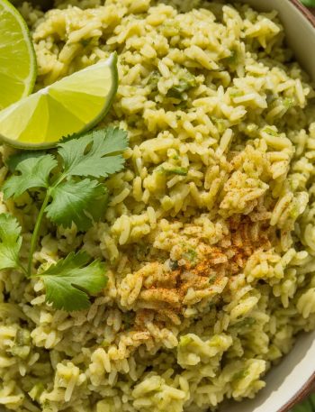 Vibrant green Mexican rice in white bowl garnished with fresh cilantro and lime wedges