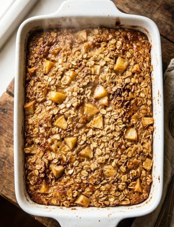 A close-up of golden Amish-style apple and cinnamon baked oatmeal in a white baking dish with tender apple chunks and a caramelized golden top