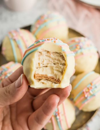 A hand holding a banana pudding Easter truffle with a bite taken out showing the creamy vanilla wafer filling inside with white chocolate coating and pastel sprinkles on top