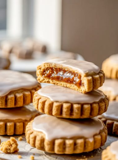 A stack of brown sugar pop tart cookies with cinnamon glaze on white parchment paper, one cookie broken in half showing the brown sugar cinnamon filling inside