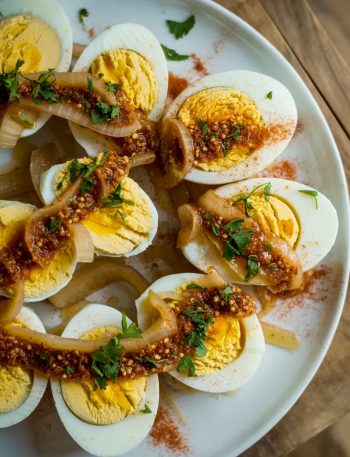 Cajun boiled eggs halved and arranged on a white plate, smothered in spicy garlic butter sauce with caramelized onions and fresh parsley garnish