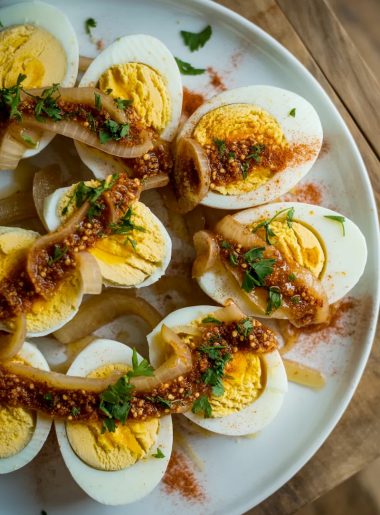 Cajun boiled eggs halved and arranged on a white plate, smothered in spicy garlic butter sauce with caramelized onions and fresh parsley garnish