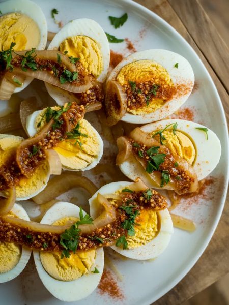 Cajun boiled eggs halved and arranged on a white plate, smothered in spicy garlic butter sauce with caramelized onions and fresh parsley garnish