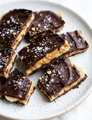 Overhead close-up of broken chocolate banana bark pieces showing peanut butter and banana layers on a white speckled plate
