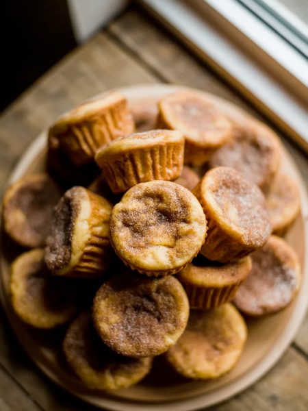A pile of golden cinnamon sugar French toast muffins with crispy coated exteriors stacked on a white ceramic plate on a wooden surface