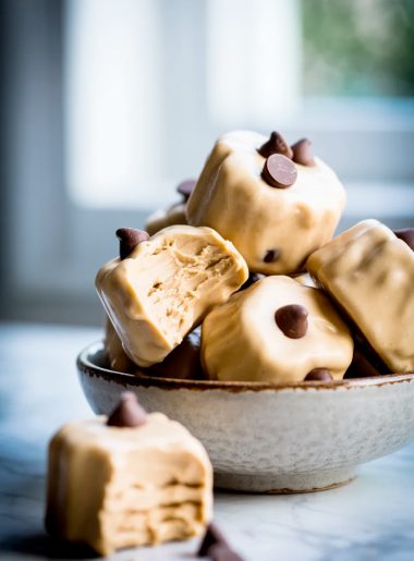 A pile of frozen Greek yogurt peanut butter bites loaded with mini chocolate chips in a ceramic bowl, one bite taken out of the front bite showing the creamy interior