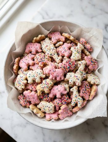 A bowl of healthy animal crackers with pink and white frosting and colorful rainbow sprinkles on a white surface