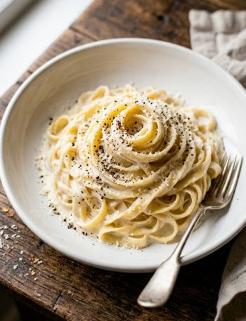 A bowl of creamy cottage cheese alfredo pasta garnished with parmesan and black pepper on a rustic wooden table