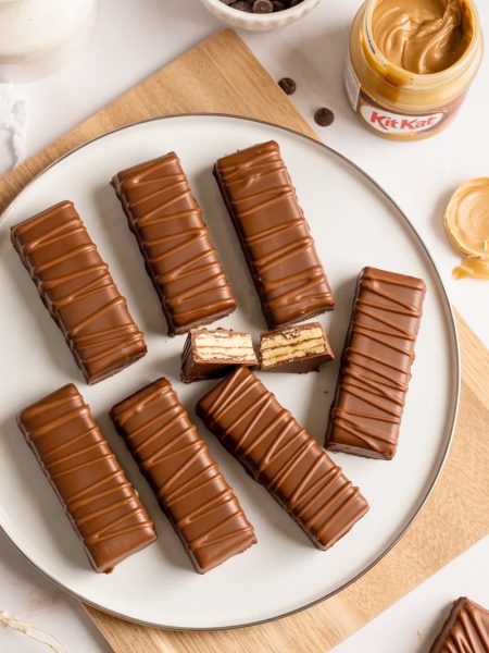 Overhead flat lay of homemade gluten free dairy free Kit Kat bars on a white ceramic plate with dark chocolate drizzle on a light wood surface