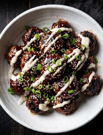 Close-up of glossy Korean BBQ meatballs in a white bowl with creamy gochujang drizzle and sliced green onions