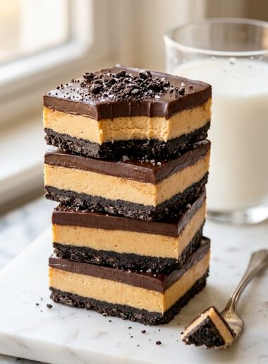 Stacked peanut butter oreo bars with chocolate topping and oreo crust on a white plate