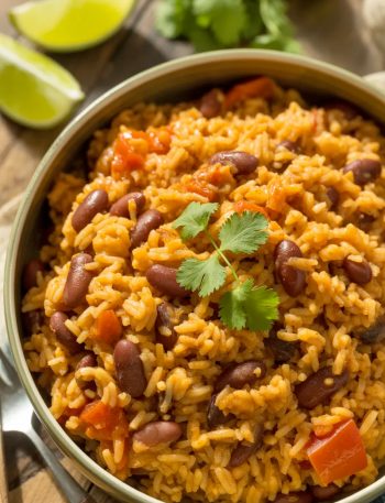 A bowl of Spanish rice and beans garnished with fresh cilantro and lime wedges on a rustic wooden table