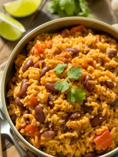 A bowl of Spanish rice and beans garnished with fresh cilantro and lime wedges on a rustic wooden table