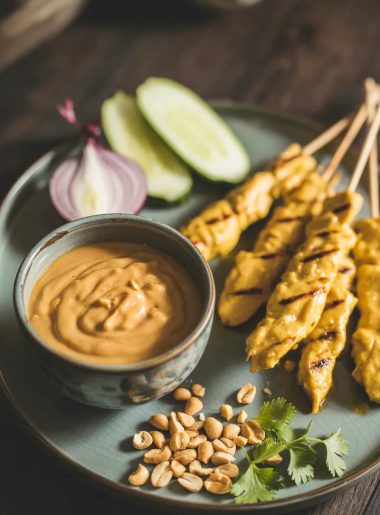 Thai chicken satay skewers served on a black plate with a bowl of homemade peanut dipping sauce garnished with crushed peanuts and fresh cilantro