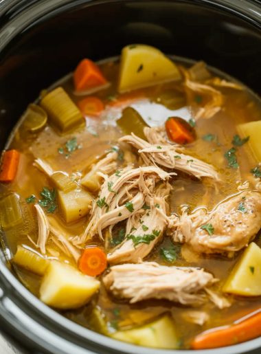 Overhead view of a crockpot filled with tender shredded chicken thigh pot roast with carrots potatoes celery and rich savory broth garnished with fresh parsley