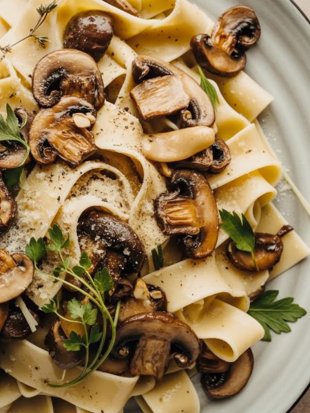 Close-up overhead shot of a large white ceramic plate piled high with garlic mushroom pappardelle pasta with golden sauteed cremini mushrooms fresh herbs and freshly grated parmesan