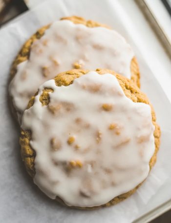 Two old fashioned iced oatmeal cookies overlapping on parchment paper with a beautiful crackled vanilla glaze finish shot from above