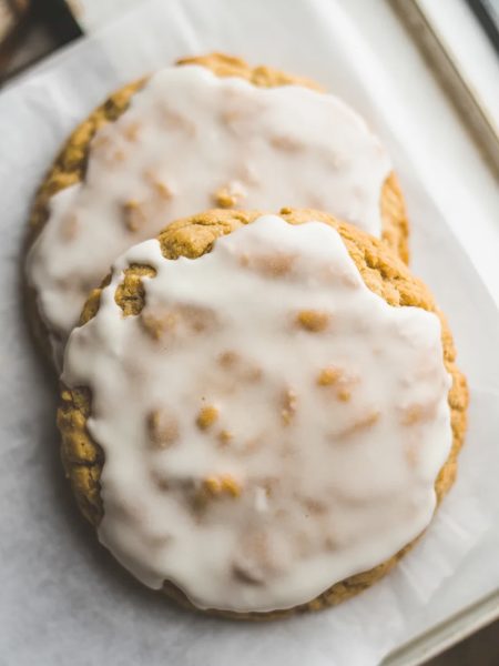 Two old fashioned iced oatmeal cookies overlapping on parchment paper with a beautiful crackled vanilla glaze finish shot from above