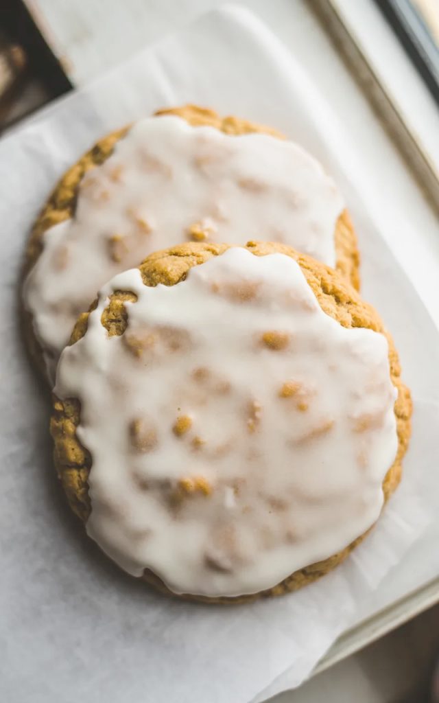 Two old fashioned iced oatmeal cookies overlapping on parchment paper with a beautiful crackled vanilla glaze finish shot from above