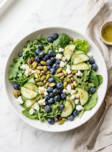 A vibrant blueberry pistachio spring salad with goat cheese, cucumber, and fresh greens in a white bowl