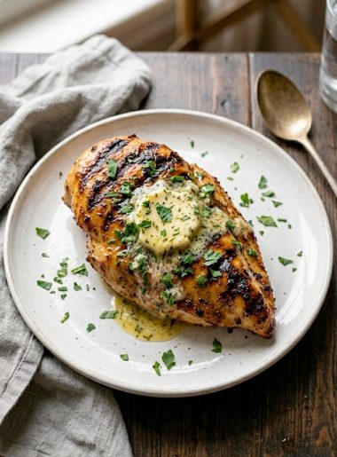 Juicy copycat Texas Roadhouse grilled chicken breast with deep grill marks herb butter melting on top and fresh parsley garnish on a white plate