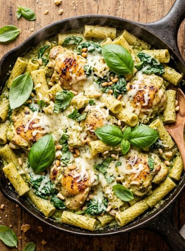 Creamy pesto chicken bake with rigatoni and spinach in a cast iron skillet garnished with fresh basil and parmesan