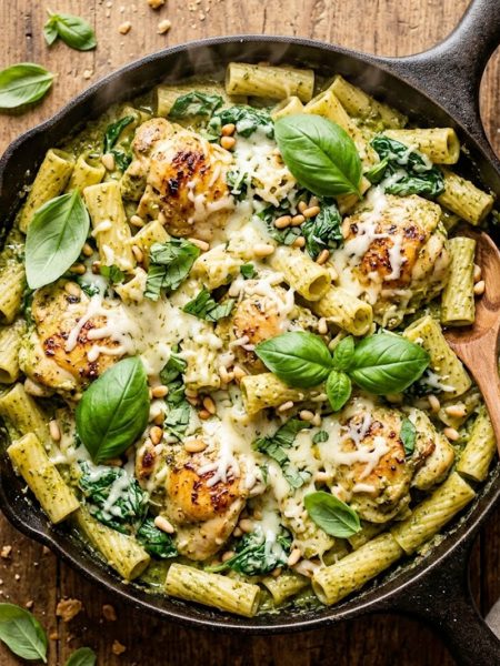 Creamy pesto chicken bake with rigatoni and spinach in a cast iron skillet garnished with fresh basil and parmesan