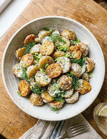A large bowl of crispy roasted potato salad tossed with fresh dill, green onions, and creamy herb dressing