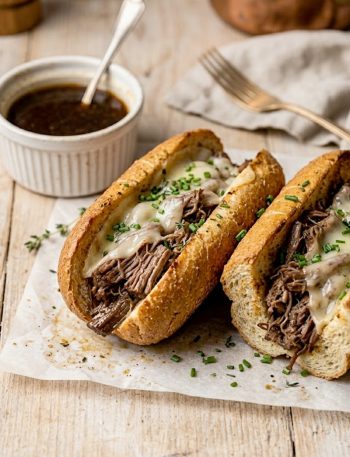 Crockpot French dip sandwiches on a wooden board with a small bowl of au jus for dipping