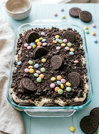 A festive Easter dirt cake casserole in a glass dish topped with colorful pastel M&Ms and whole Oreo cookies on a light spring table setting