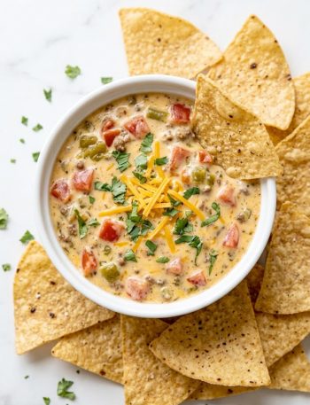Overhead view of creamy Rotel cheese dip in a white ramekin garnished with cilantro and surrounded by tortilla chips on a marble surface