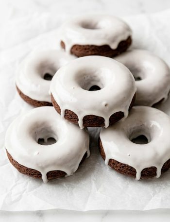Easy chocolate cake donuts with vanilla glaze stacked on parchment paper with glaze dripping down the sides